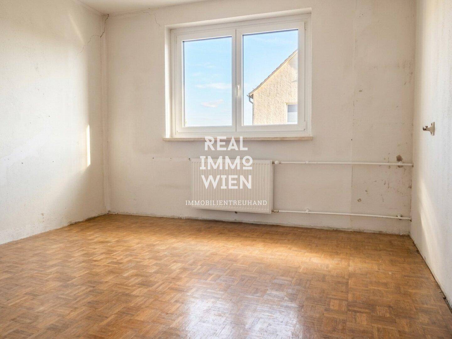 Leeres Zimmer mit Parkettboden und Fenster, bereit für die individuelle Gestaltung und Renovierung.