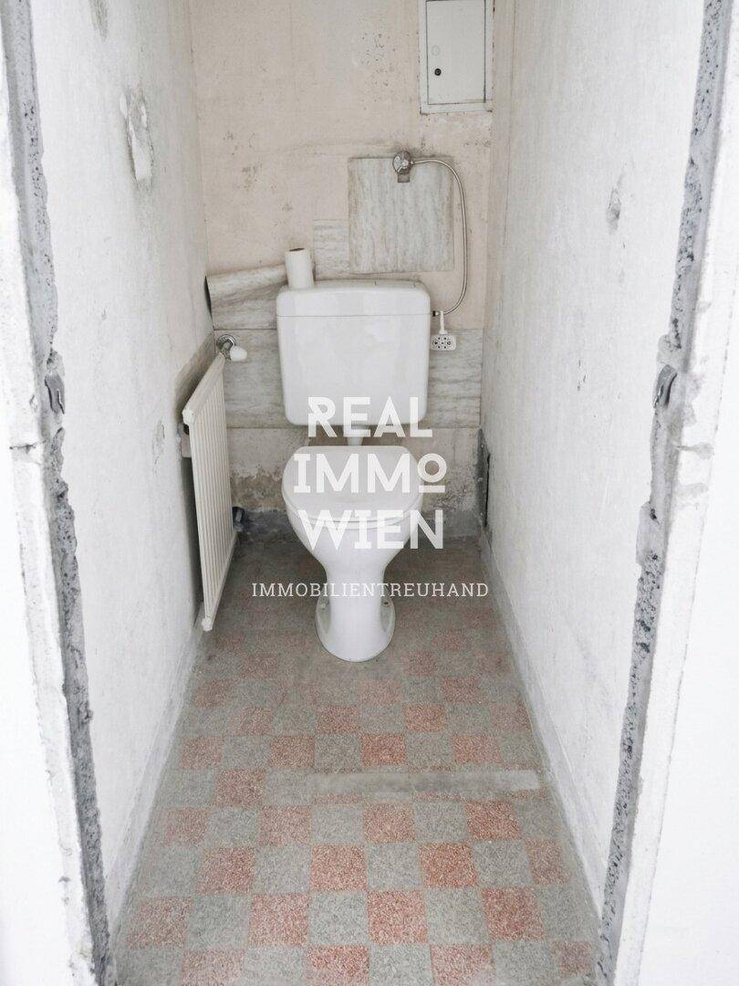 Einfache separate Toilette mit Fliesenboden und Heizkörper, benötigt eine Modernisierung.