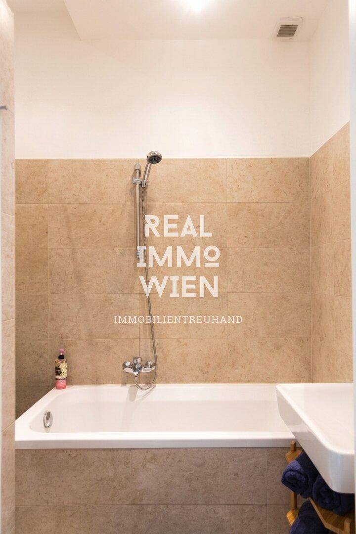 Badezimmer mit Badewanne und Duscharmatur, ausgestattet mit beigefarbenen Fliesen für ein klassisches Ambiente.