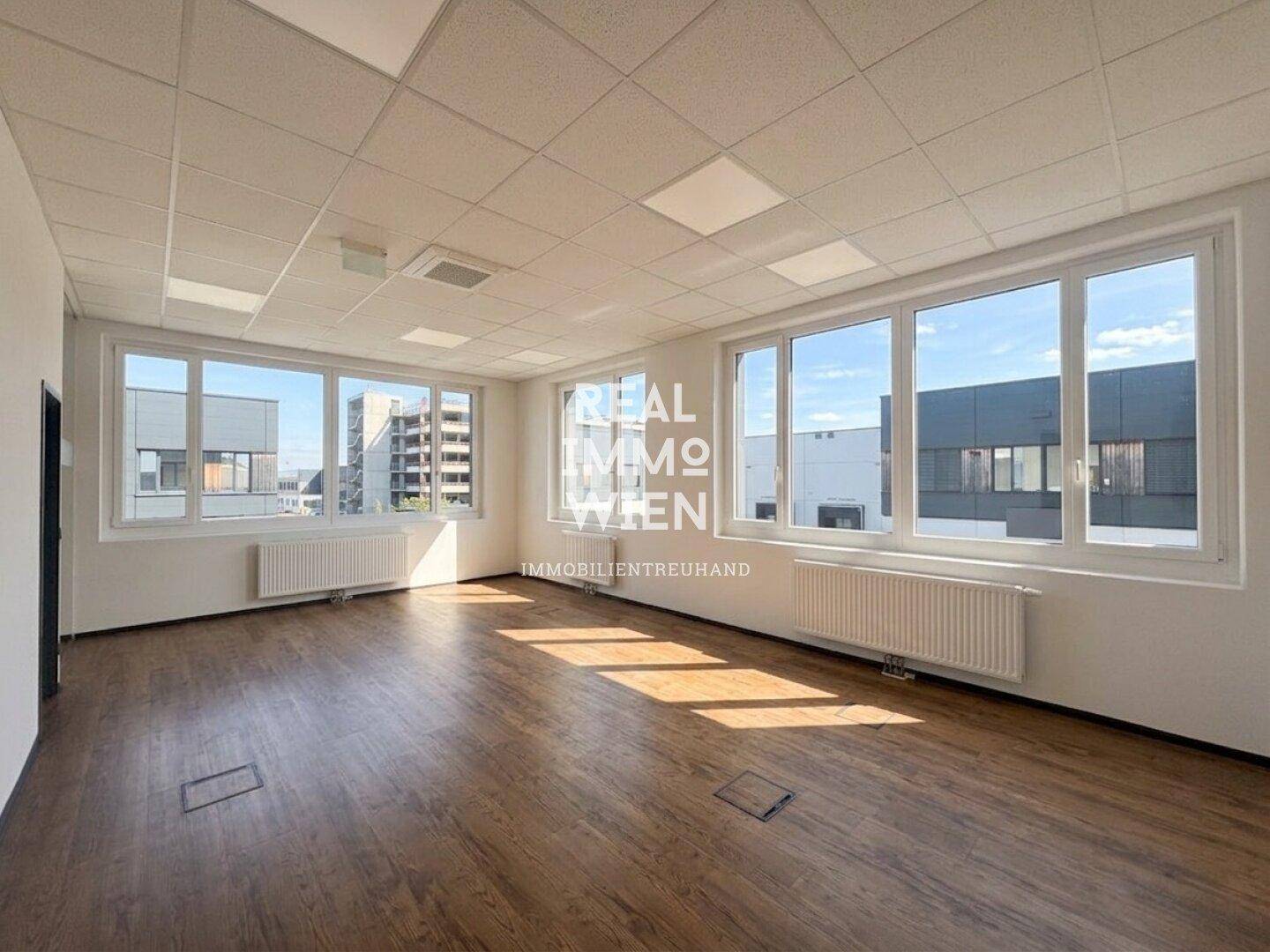 Großer, leerer Büroraum mit vielen Fenstern und einem modernen Laminatboden.