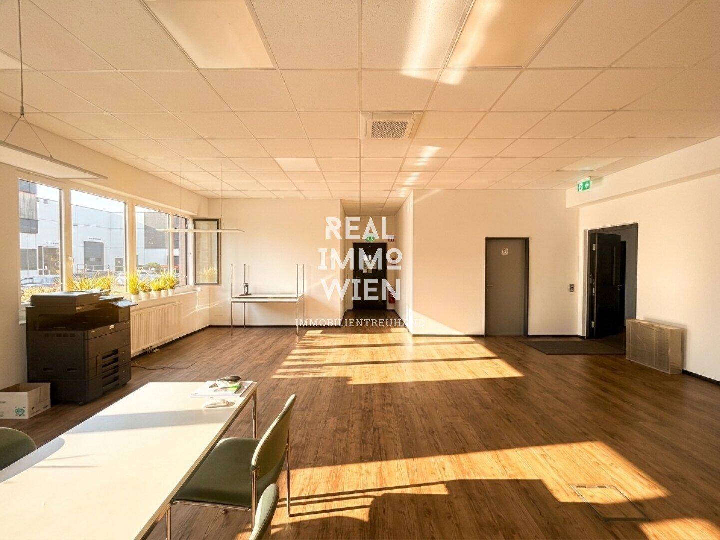 Heller Büroraum mit großen Fenstern, Holzboden und abgehängter Decke.
