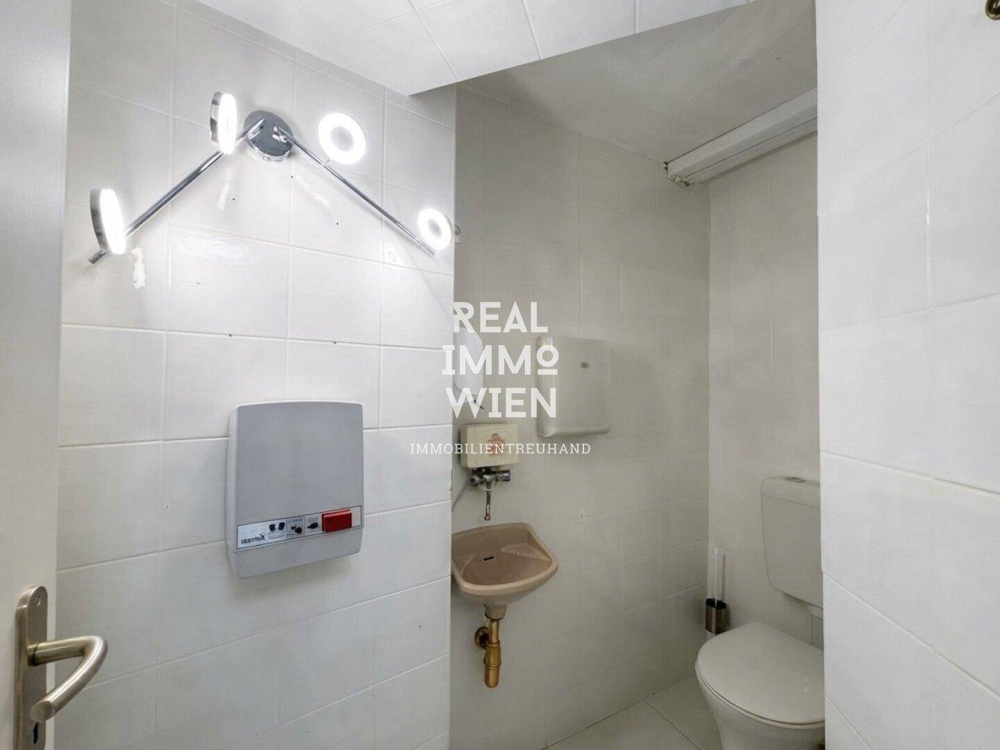Einfache Toilette mit Wandfliesen, kleinem Waschbecken und Spender, funktional und sauber gehalten.