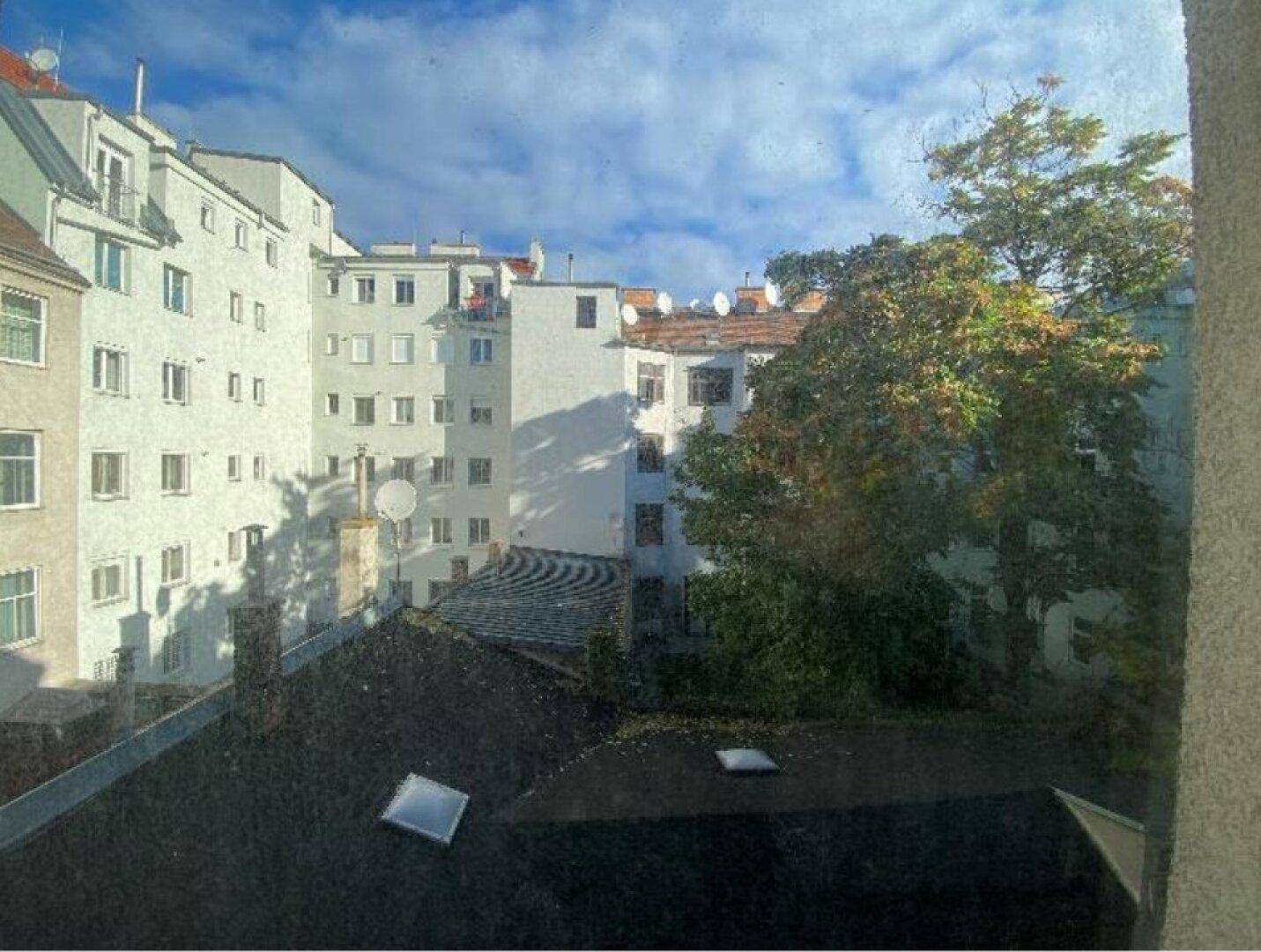 Blick aus dem Fenster auf einen begrünten Innenhof mit umliegenden Gebäuden und Dächern.
