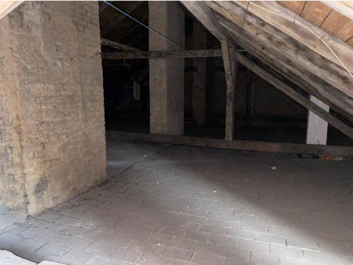 Unausgebauter Dachbodenbereich mit sichtbaren Holzbalken und Ziegelwänden.