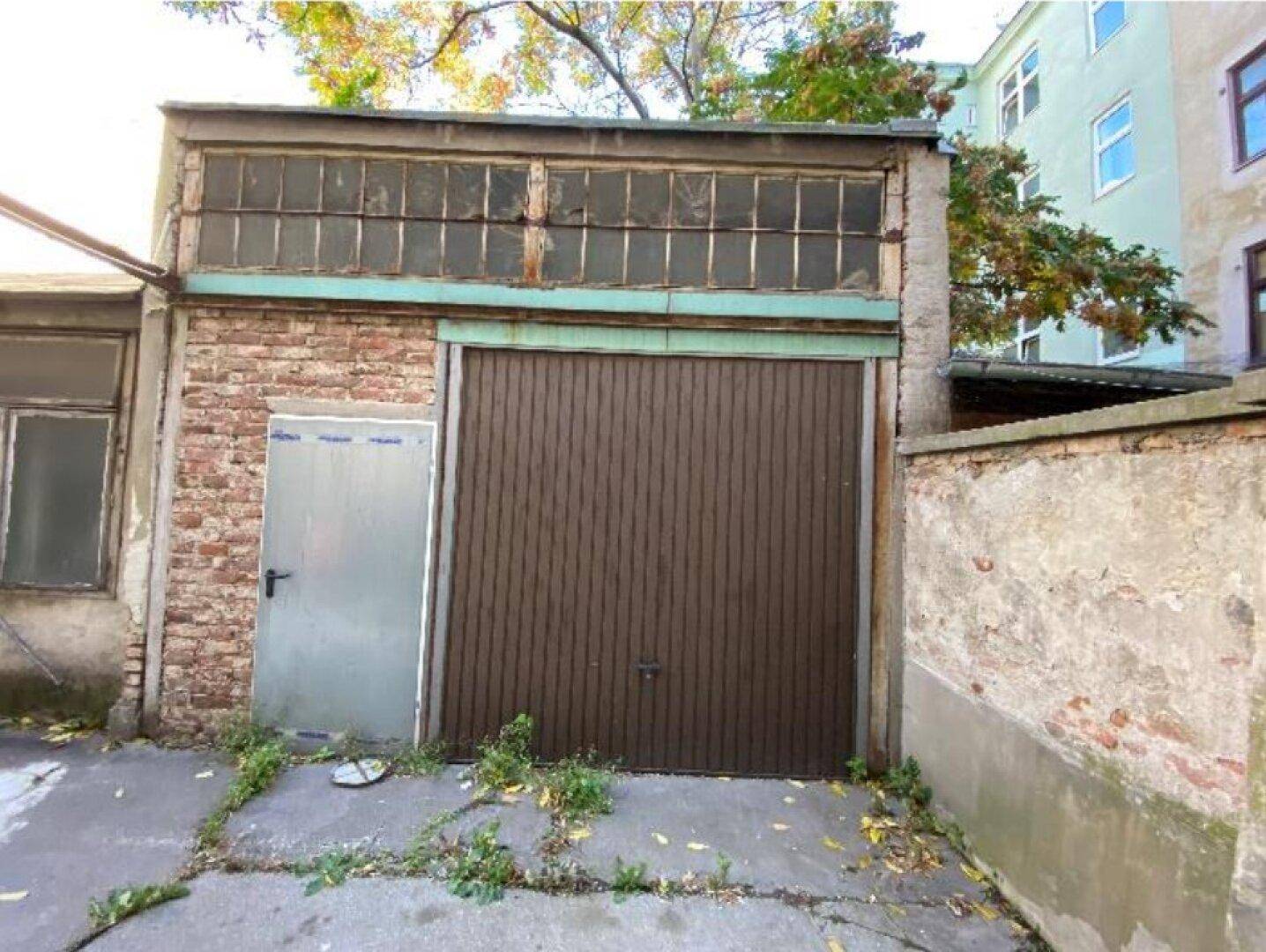 Einzelne Garage mit Holztor und Ziegelwänden in einem Hinterhofbereich.