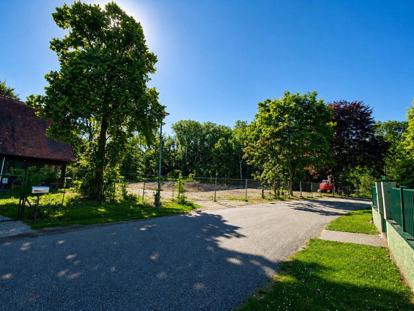 Sonniges Baugrundstück mit umliegendem Grün und angrenzender Straße, ideal für Neubauprojekte.