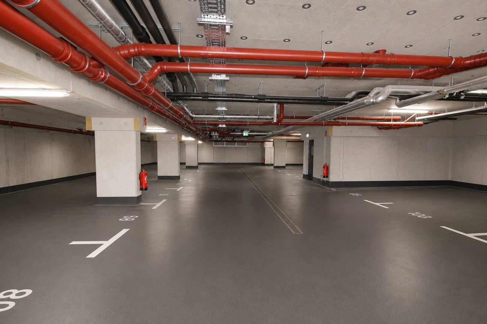 Geräumige Tiefgarage mit markierten Parkplätzen und sichtbaren Versorgungsleitungen an der Decke.