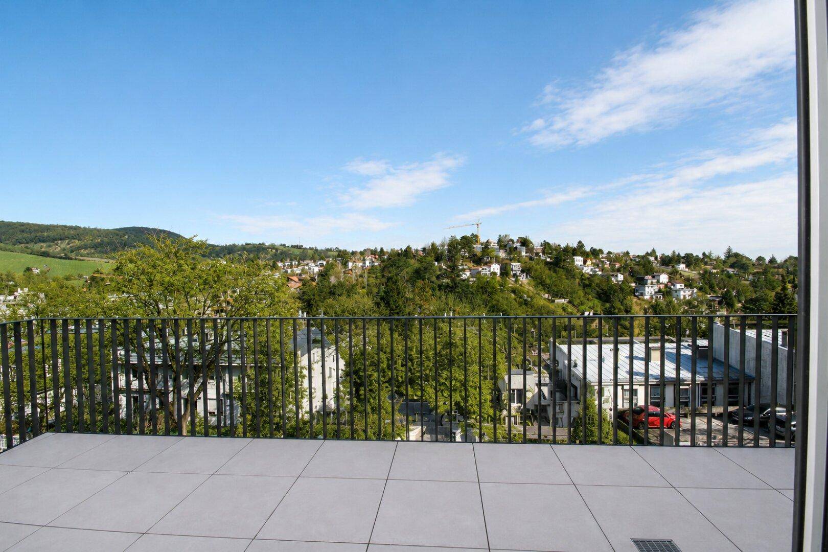 Balkon mit Fliesenboden und Panoramablick auf die umliegende Stadt und grüne Hügel.