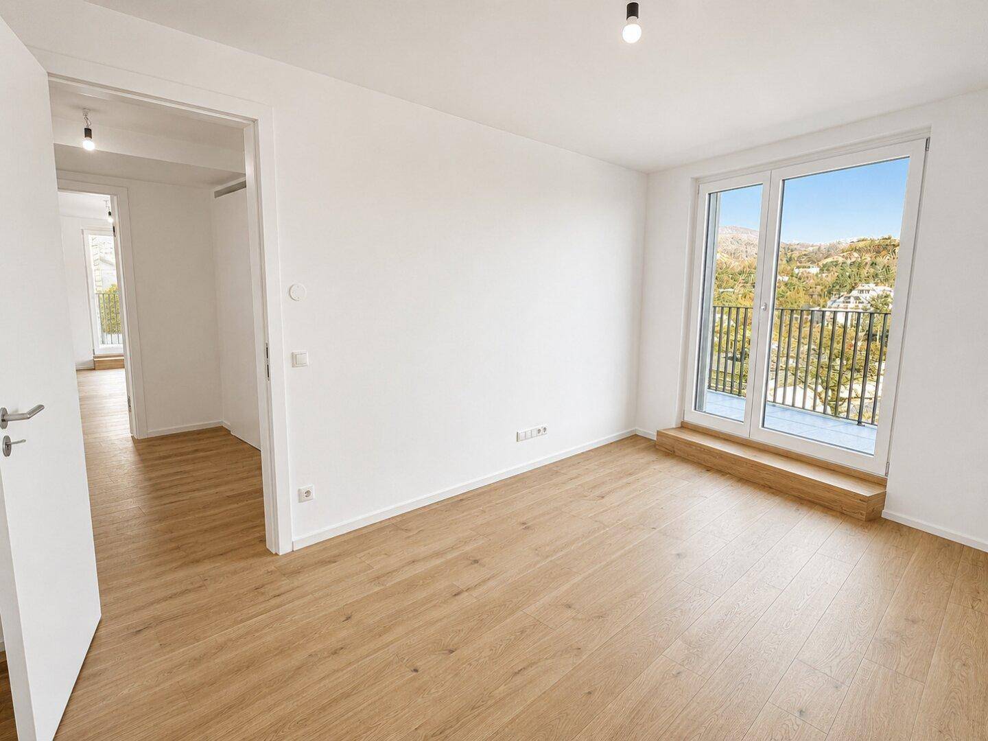 Leeres Schlafzimmer mit Holzboden und Zugang zu einem Balkon, bietet viel natürliches Licht.