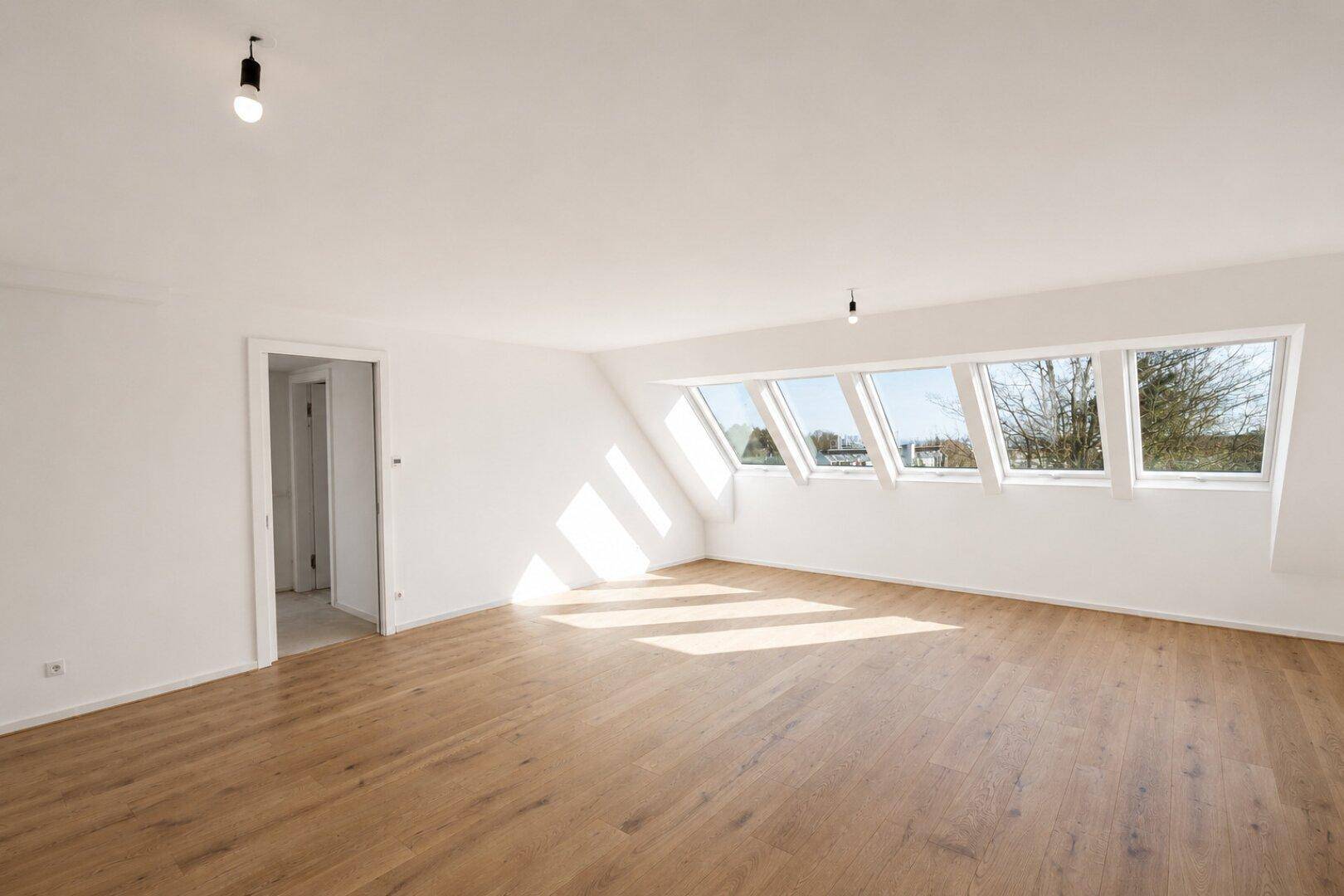 Heller Wohnraum im Dachgeschoss mit Holzboden, großen Dachfenstern und viel natürlichem Licht.