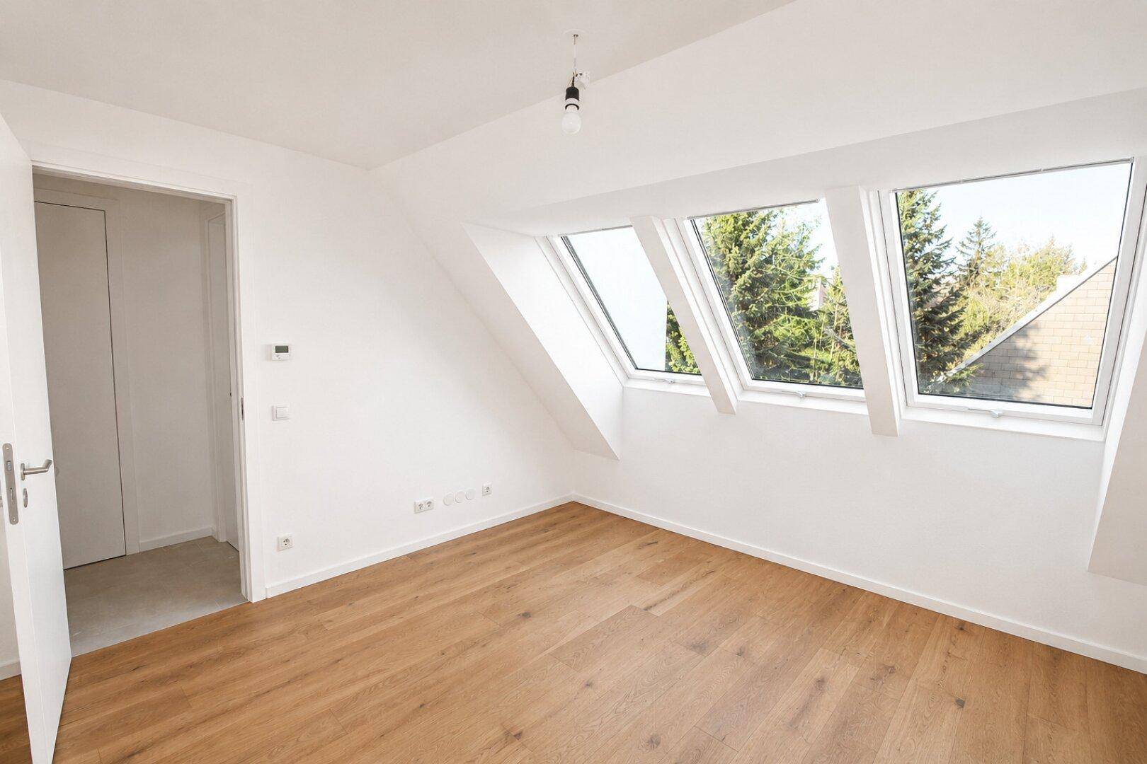 Schlafzimmer im Dachgeschoss mit Holzboden, schrägen Wänden und großen Dachfenstern.