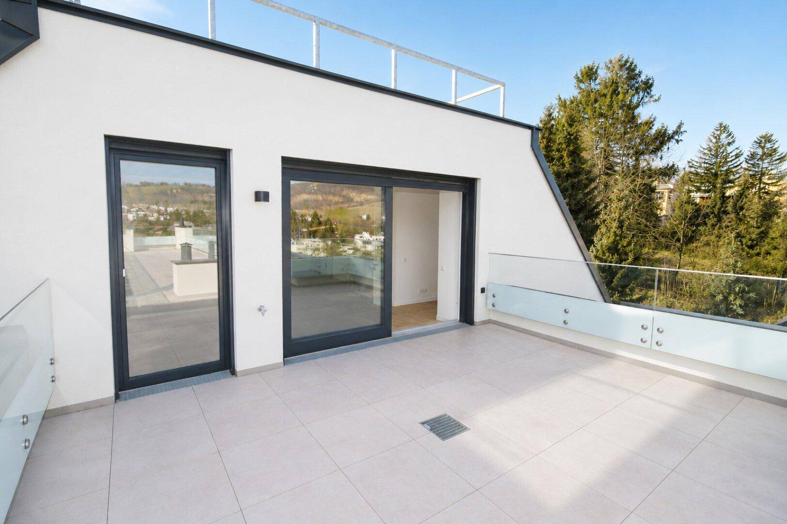 Geräumige Terrasse mit modernen Glasgeländern und Zugang zu den Innenräumen.