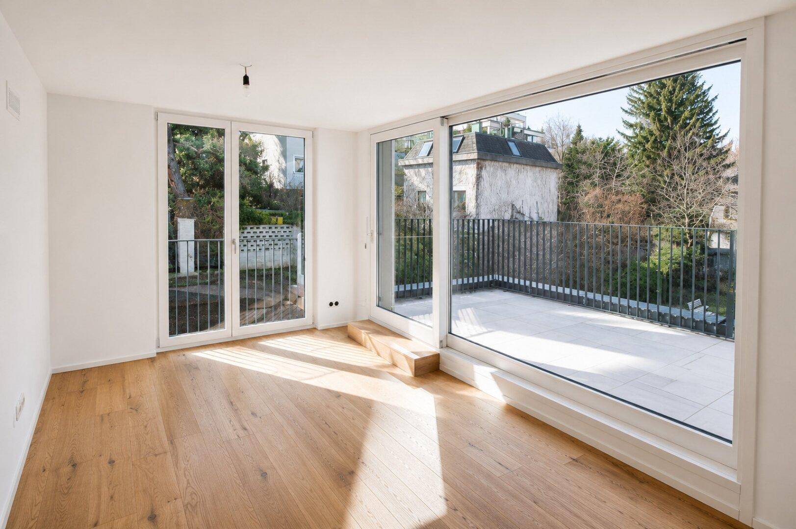 Lichtdurchfluteter Raum mit Holzboden und großen Fenstern, die auf eine Außenterrasse blicken.