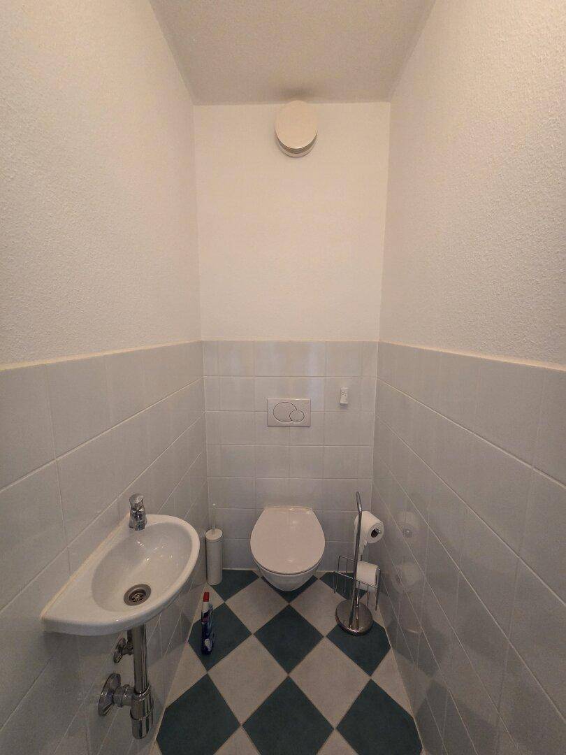 Separates Gäste-WC mit Wand-WC, kleinem Waschbecken und auffälligem Schachbrettmuster-Boden.