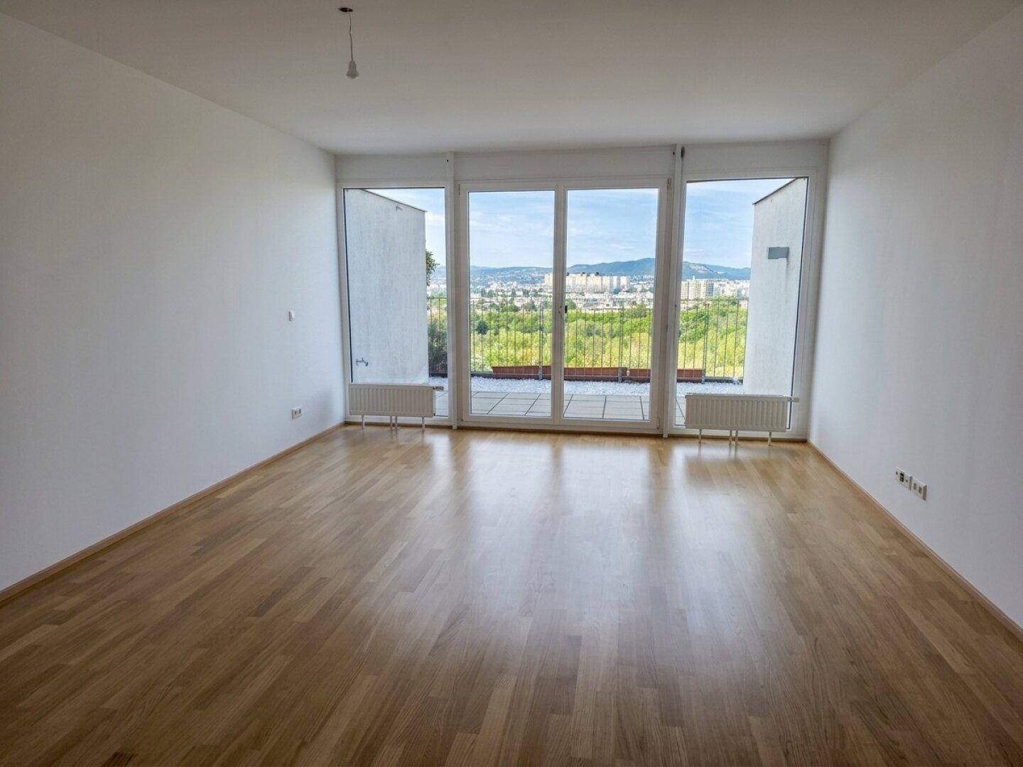 Helles Wohnzimmer mit Parkettboden, großen Fenstern und Zugang zu einem Balkon mit Weitblick.