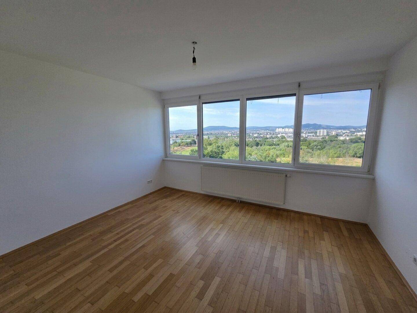 Helles Schlafzimmer mit Parkettboden und breiten Fenstern, die einen schönen Ausblick bieten.