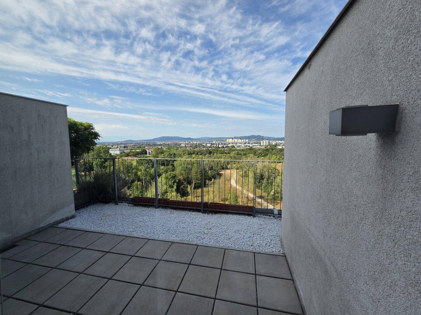 Geräumige Terrasse mit Steinplatten und Kies, umgeben von einem Geländer mit Panoramablick.