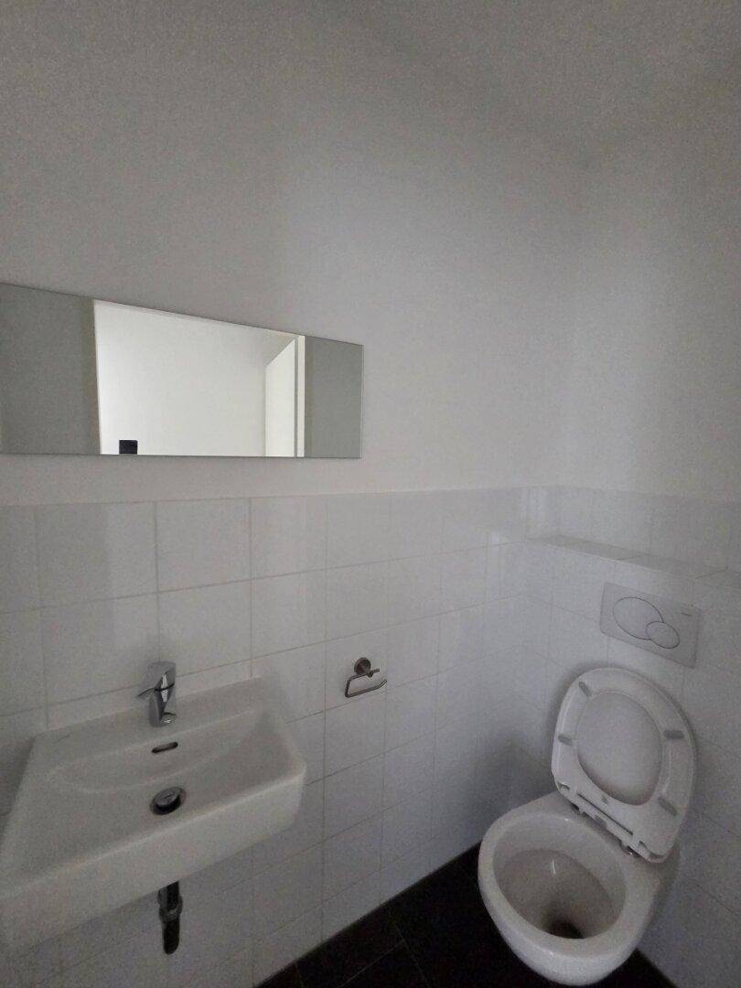 Kleines Gäste-WC mit weiß gefliesten Wänden, einem Waschbecken und einem Wandspiegel.