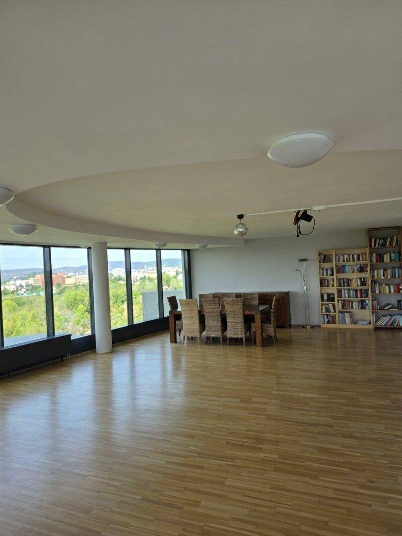 Geräumiger Wohn-Essbereich mit Holzboden, raumhohen Fenstern und einem Bücherregal mit Panoramablick.