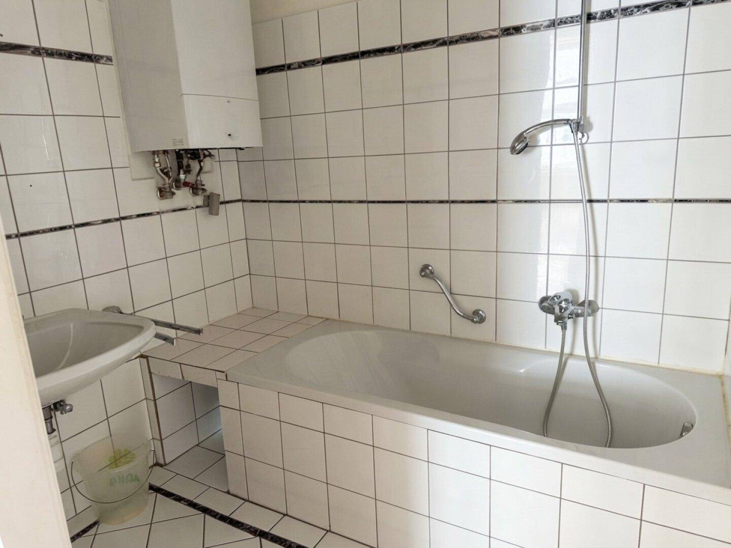 Badezimmer mit weiß gefliesten Wänden, Badewanne und Handläufen für mehr Sicherheit.