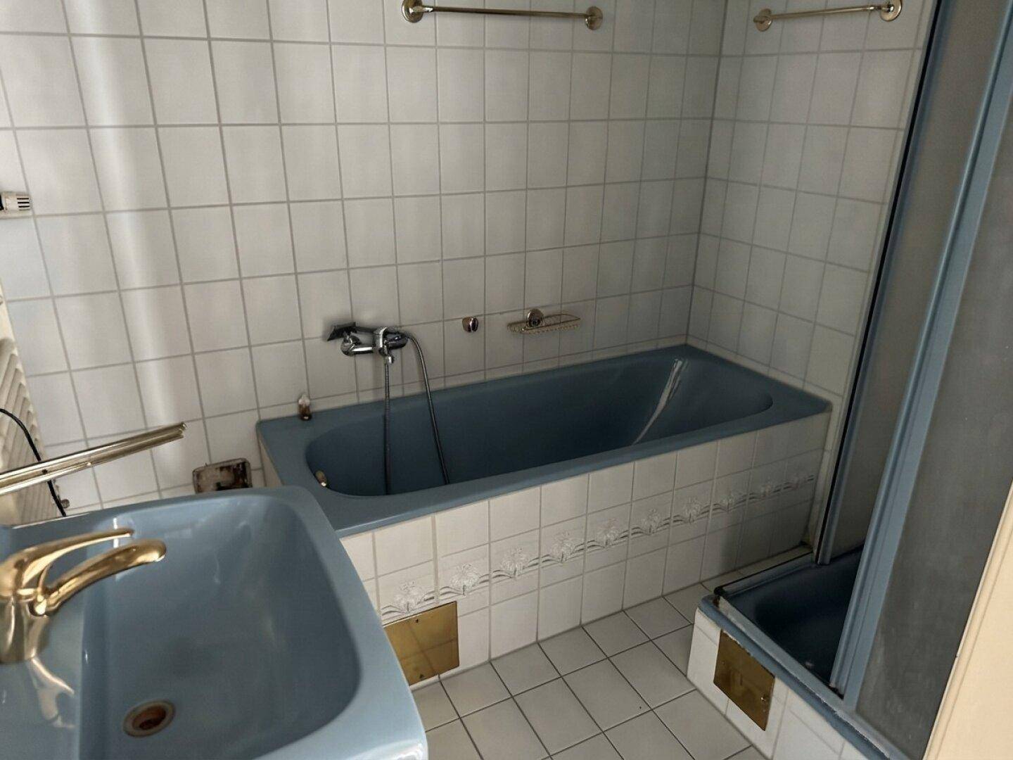Badezimmer mit blauer Badewanne und Waschbecken, umgeben von weißen Fliesen.