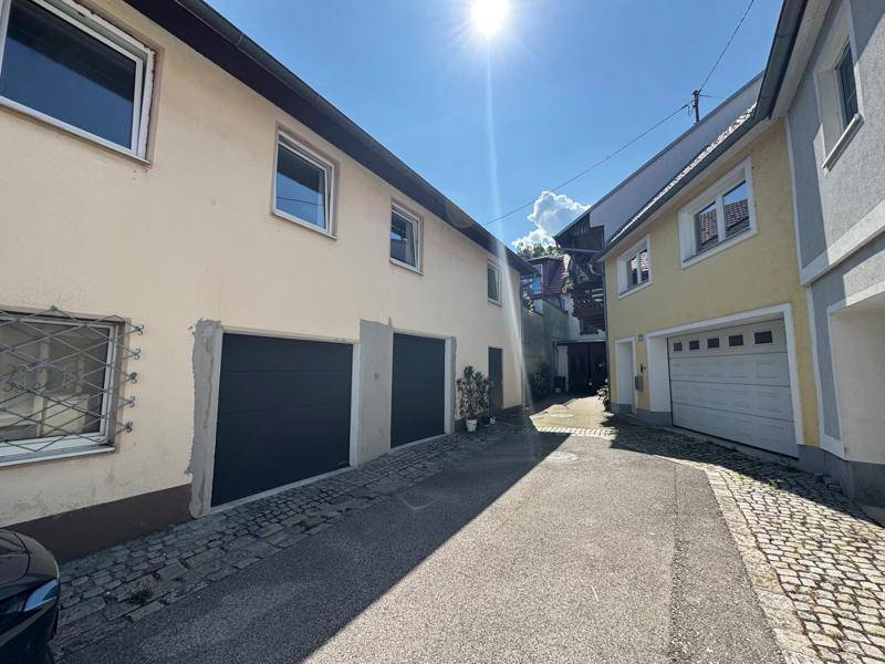 Schmale Gasse zwischen Gebäuden mit Garagentoren, die zu einem Innenhof führt.