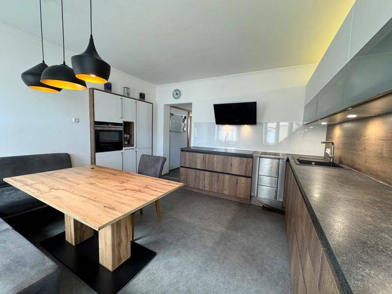 Moderne offene Küche mit Essbereich, Holzelementen, dunklen Arbeitsplatten und Hängelampen.