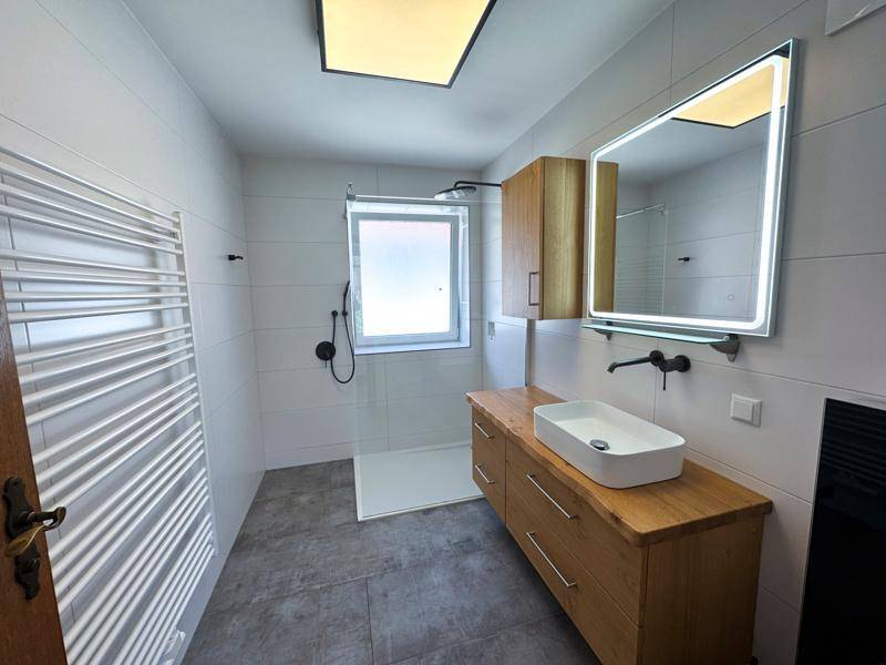 Modernes Badezimmer mit ebenerdiger Dusche, Holzwaschtisch, beheiztem Handtuchhalter und Fenster.