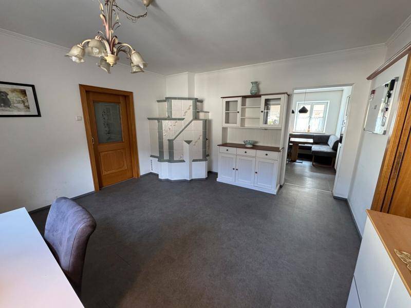 Helles Wohnzimmer mit traditionellem Kachelofen, Vinylboden und einem eleganten Schrank.