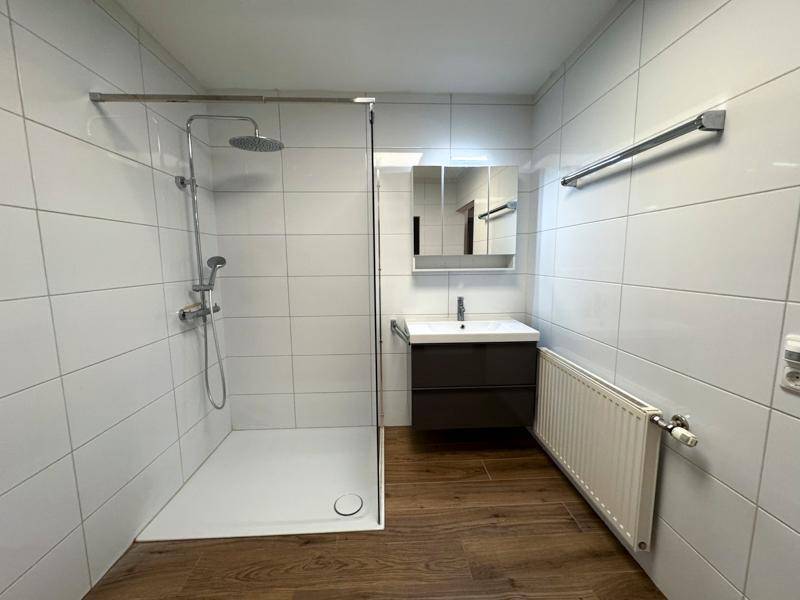 Helles Badezimmer mit ebenerdiger Dusche, weißen Fliesen und einem modernen Waschtisch.