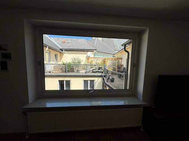 Blick aus dem Fenster auf die private Terrasse mit Sitzgelegenheiten und umliegenden Gebäuden.