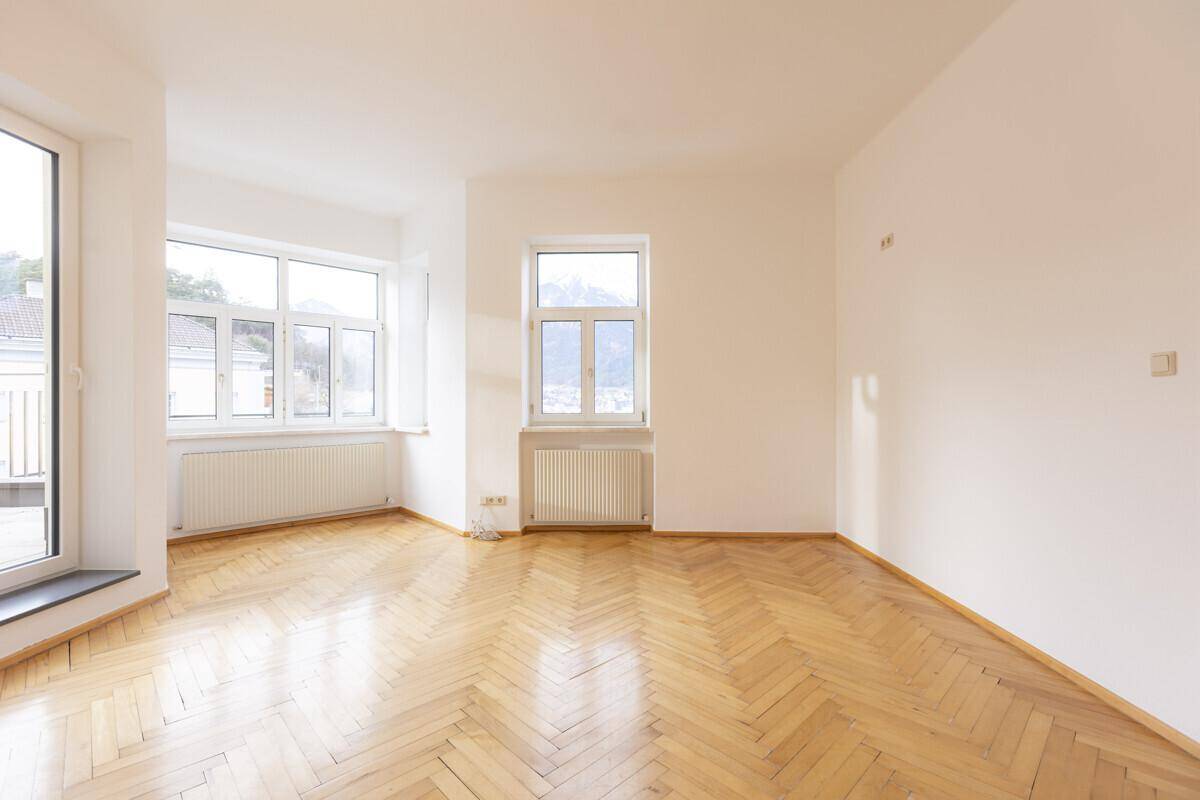 Helles Wohnzimmer mit Fischgrätparkett, großen Fenstern und Zugang zum Balkon.