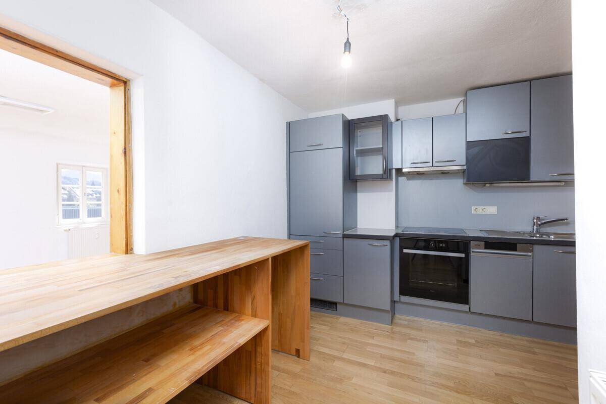 Moderne Küche mit grauen Schränken, integrierten Geräten und einer Holz-Frühstücksbar.