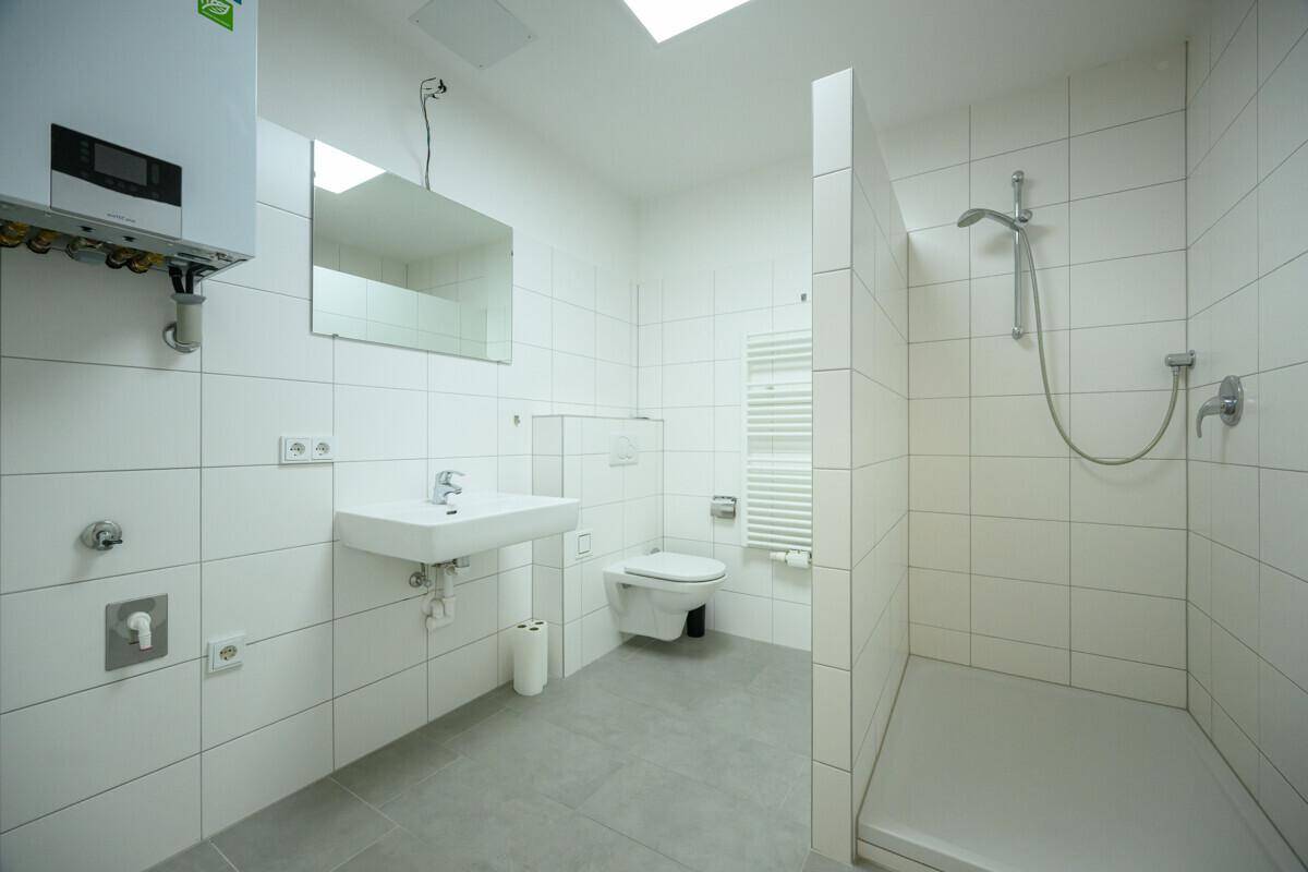 Modernes Badezimmer mit weißen Fliesen, ebenerdiger Dusche und Wand-WC.