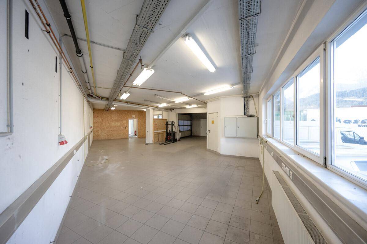 Geräumiger Lager- oder Arbeitsbereich mit großen Fenstern, Fliesenboden und sichtbaren Deckeninstallationen.