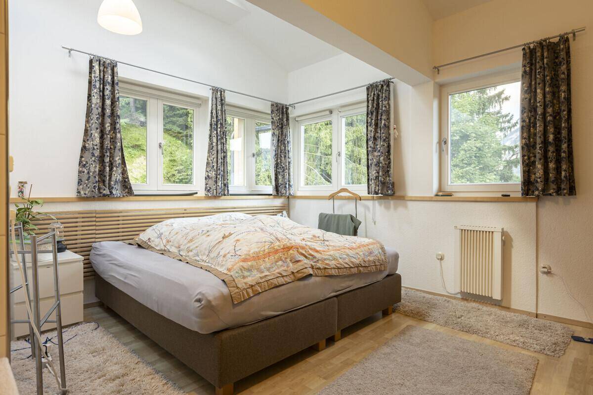 Geräumiges Schlafzimmer mit Doppelbett, Holzboden und mehreren Fenstern mit Blick ins Grüne.