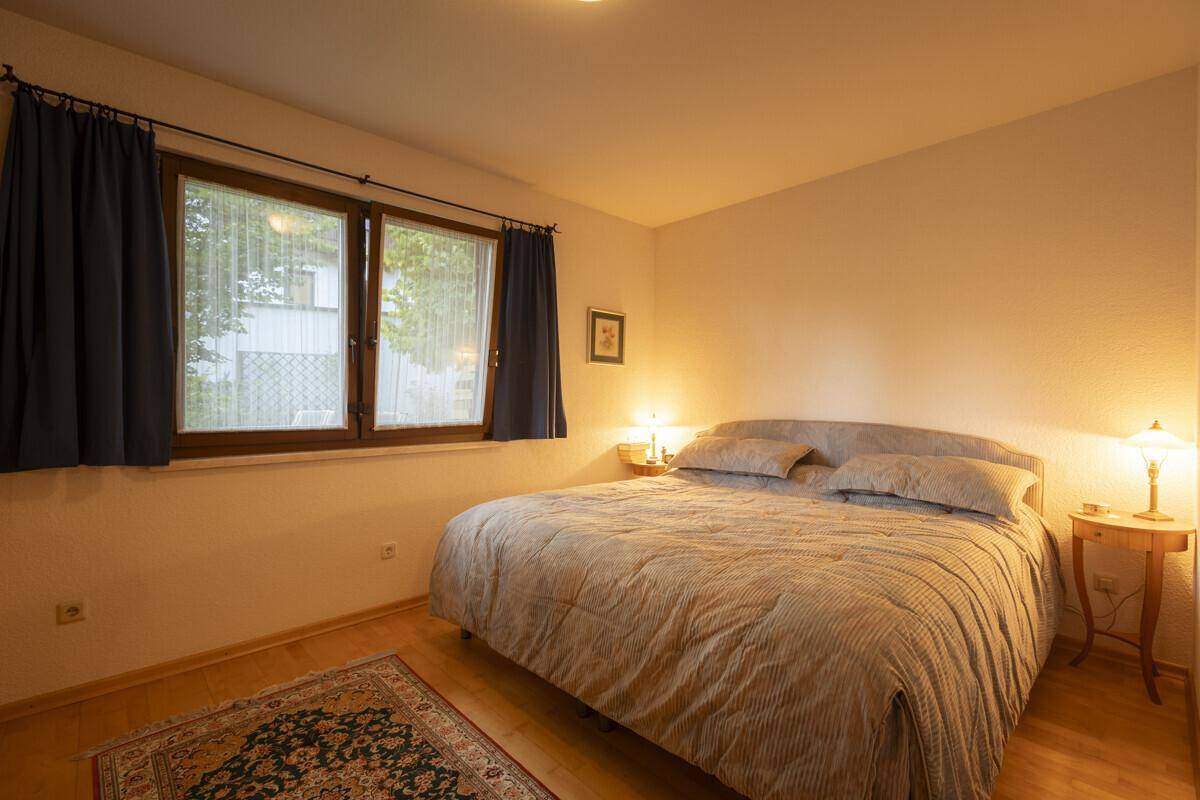Gemütliches Schlafzimmer mit Doppelbett, Holzboden und Fenster mit Vorhängen.