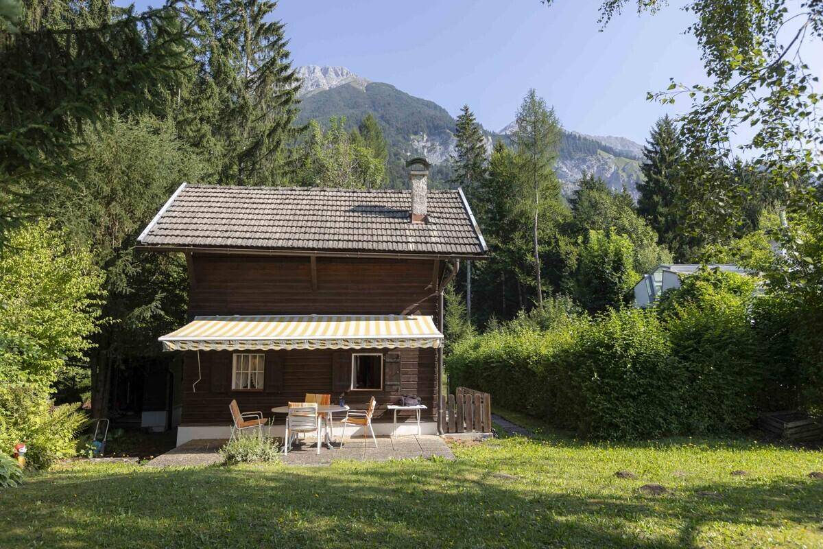 Charmantes Holzhaus mit Terrasse und Bergblick, umgeben von grünen Bäumen und Natur.