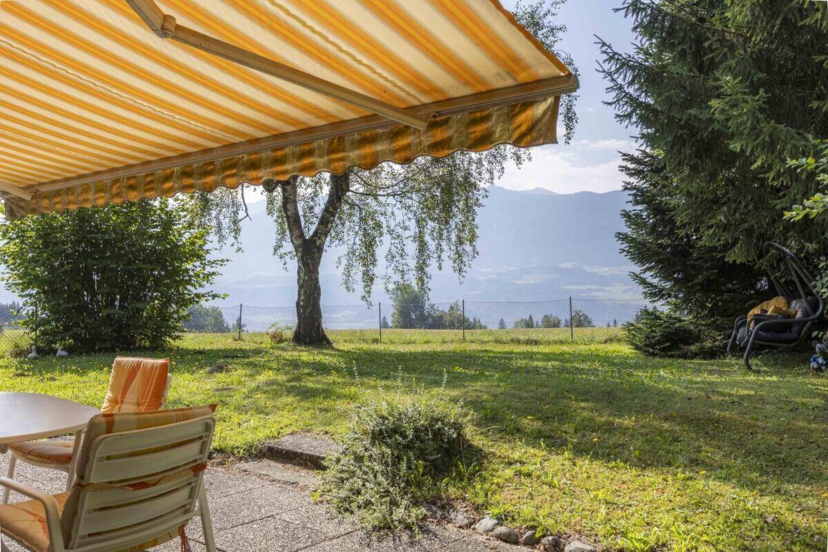 Sonnige Terrasse mit Markise und weitem Blick über grüne Felder und majestätische Berge.