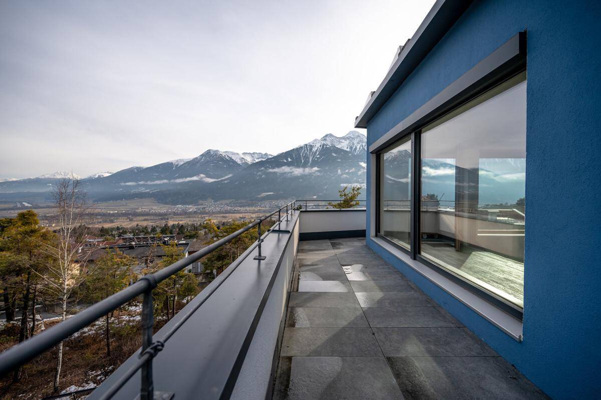 Große Terrasse mit Bergblick und blauer Fassade des Gebäudes.
