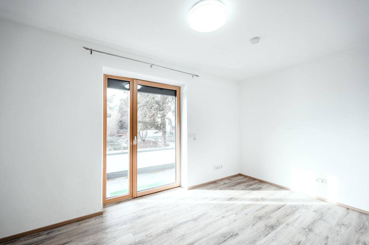 Freundliches Schlafzimmer mit großen Fenstern, viel Tageslicht und hellem Laminatboden.