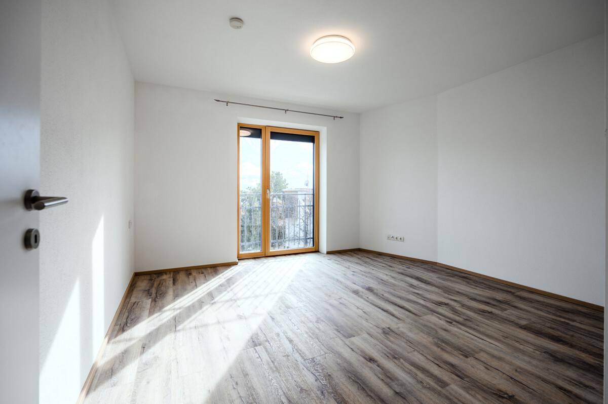 Helles Schlafzimmer mit Holzboden und Zugang zu einem kleinen Balkon oder einer Terrasse.