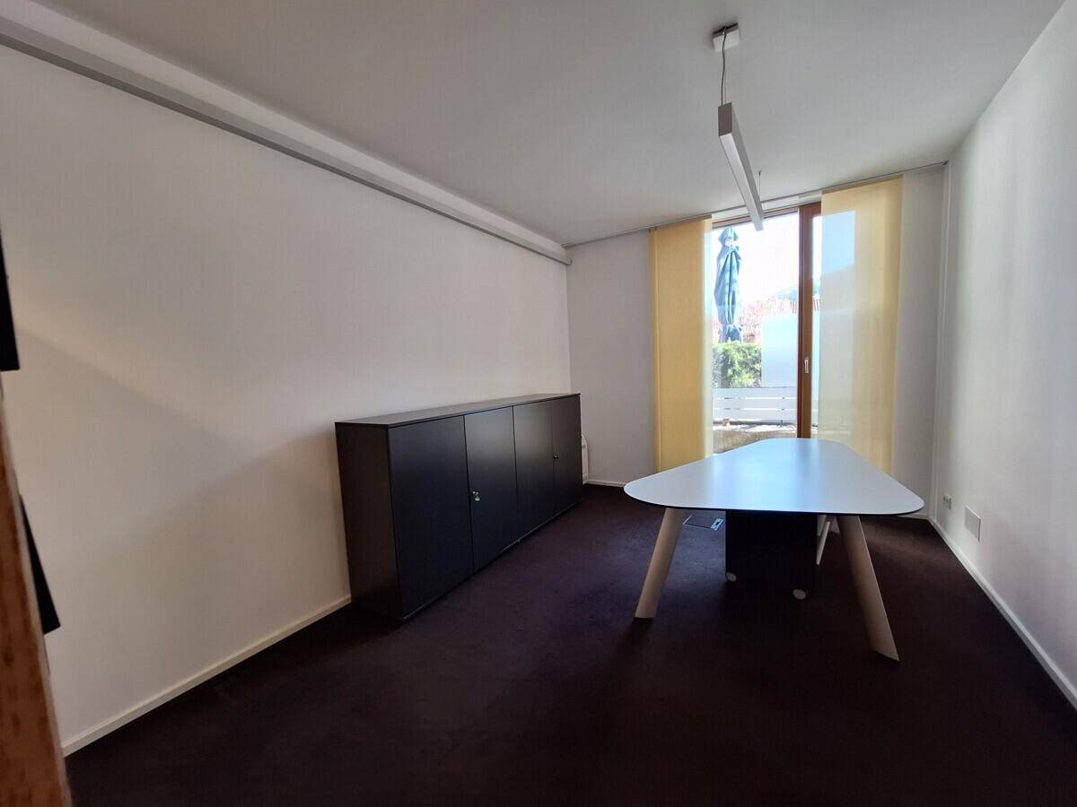 Helles Büro mit modernem Tisch, dunklem Schrank und Fenster mit Blick nach draußen.