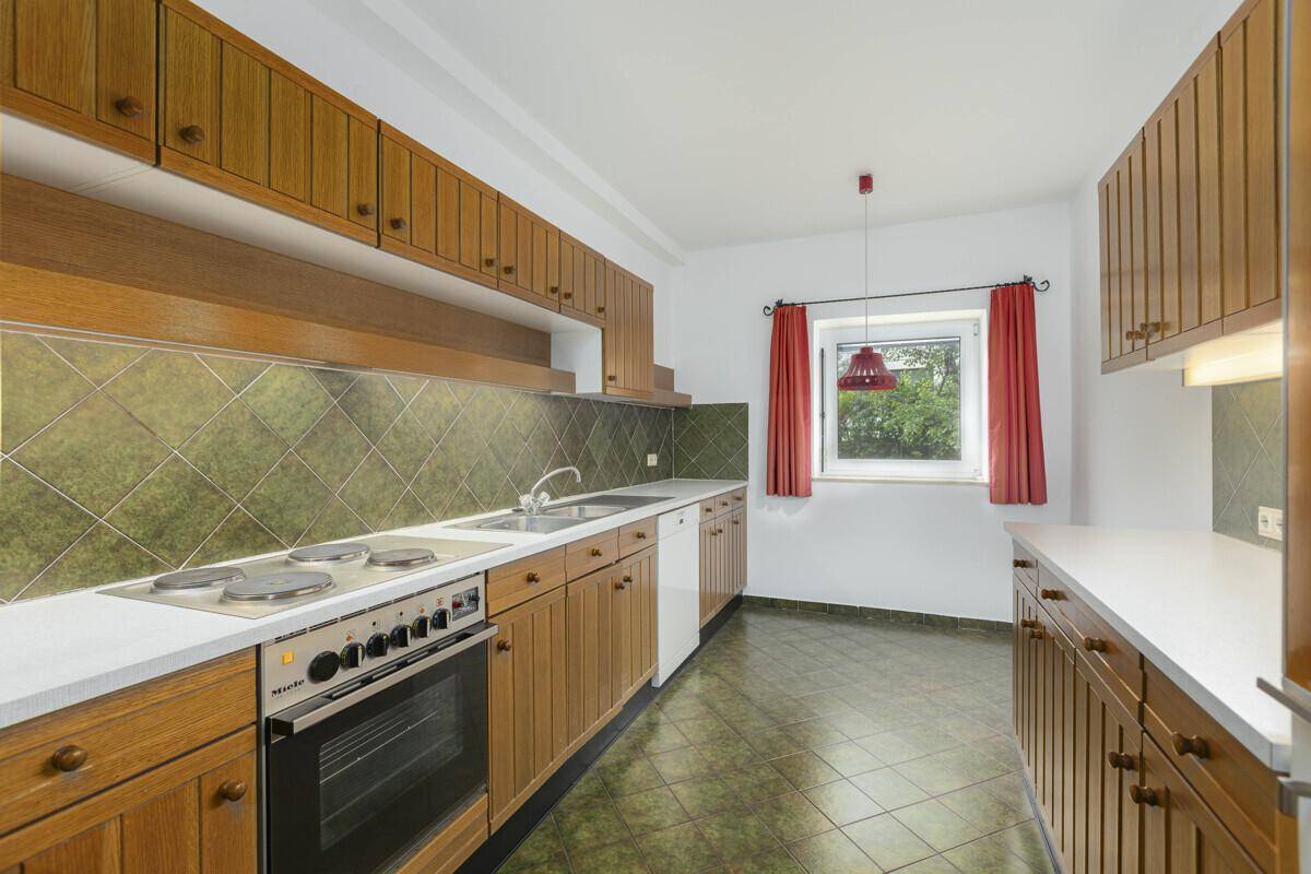 Traditionelle Küche mit Holzschränken, grünen Fliesen und einem Fenster mit Blick ins Grüne.