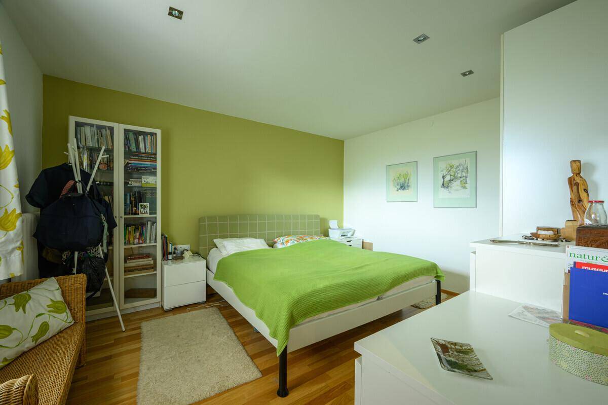 Helles Schlafzimmer mit grün gestrichener Wand, Holzboden und einem großen Bett mit grüner Decke.