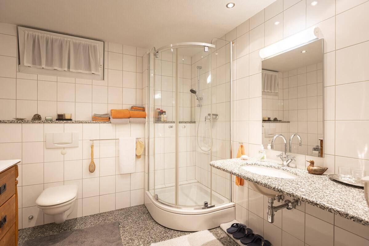 Modernes Badezimmer mit Duschkabine, weißen Fliesen und Granit-Waschtisch.