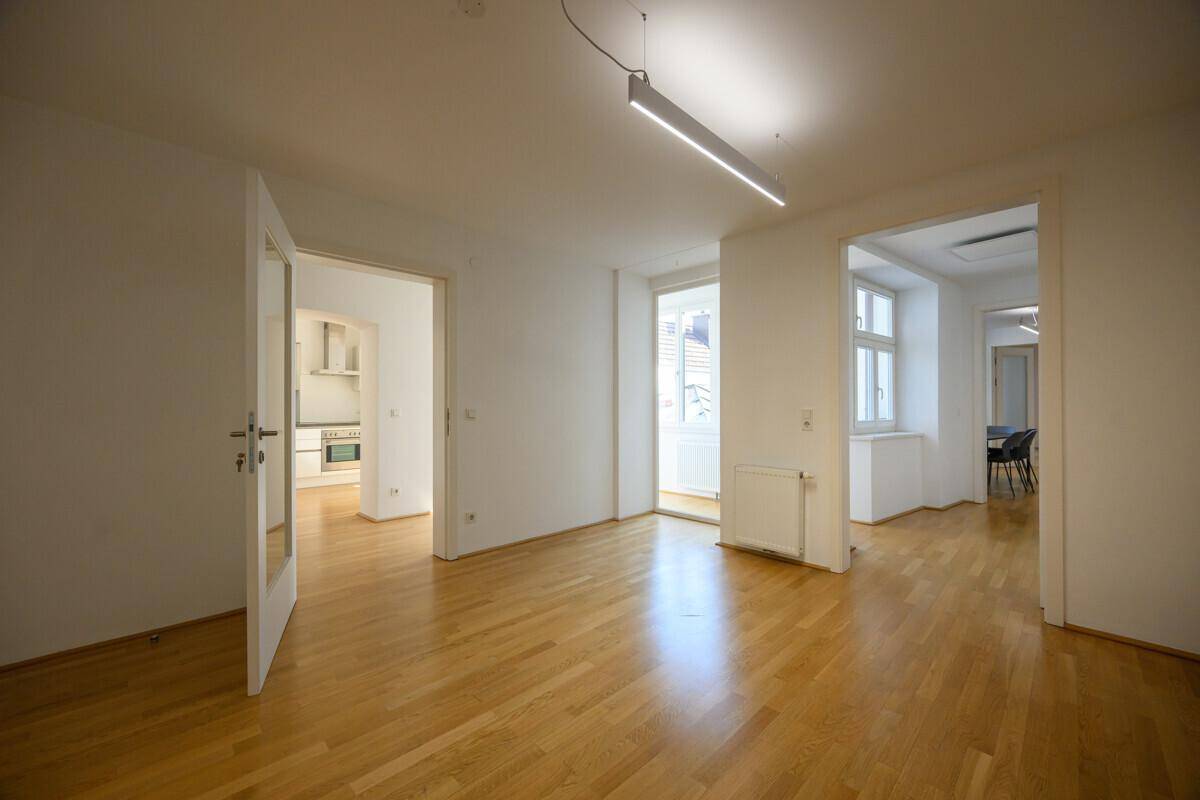 Heller, offener Raum mit Holzboden und Zugang zu mehreren Zimmern, inklusive Küche.