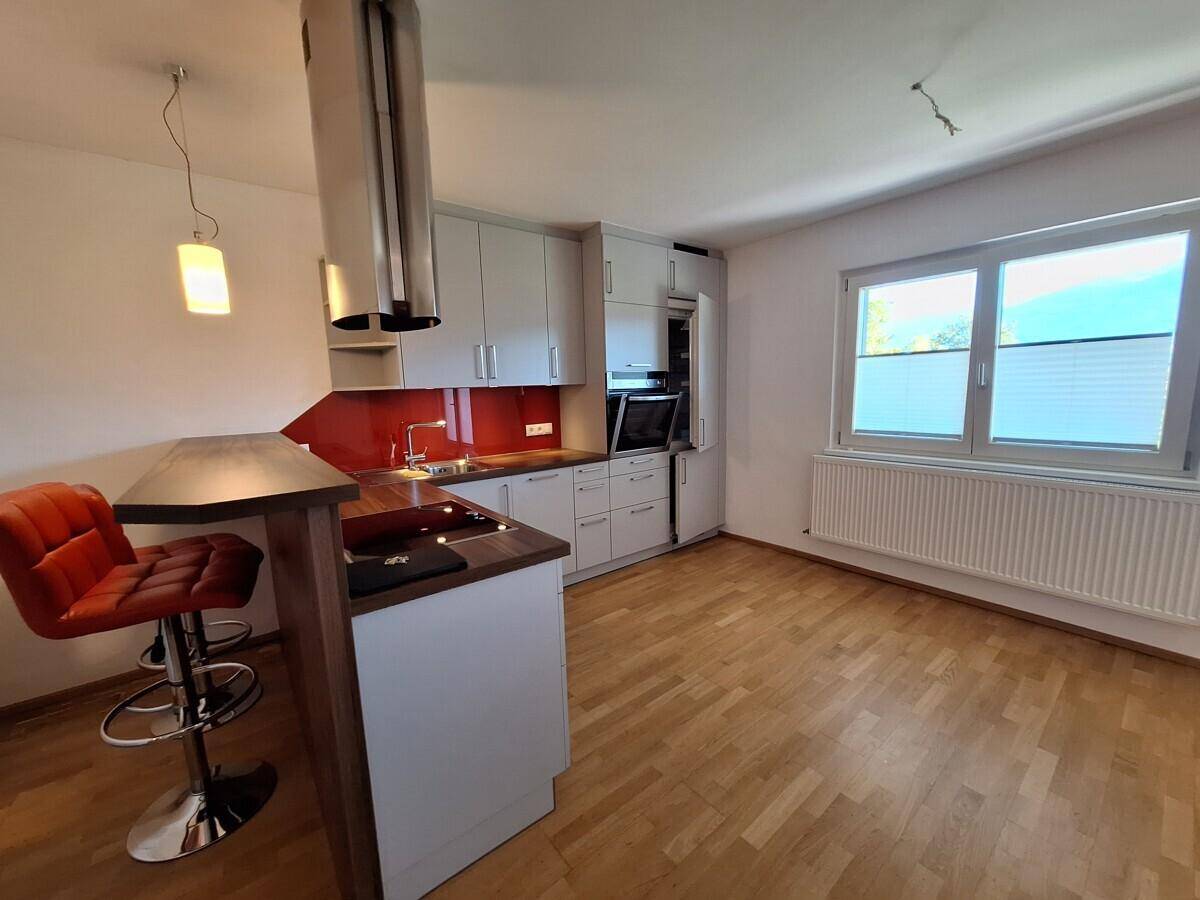 Moderne Küche mit grauen Schränken, roter Rückwand, Kochinsel und Barhockern.
