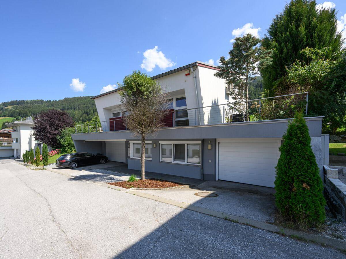 Modernes Wohnhaus mit Garagen, Carport und Balkonen in bergiger Umgebung.