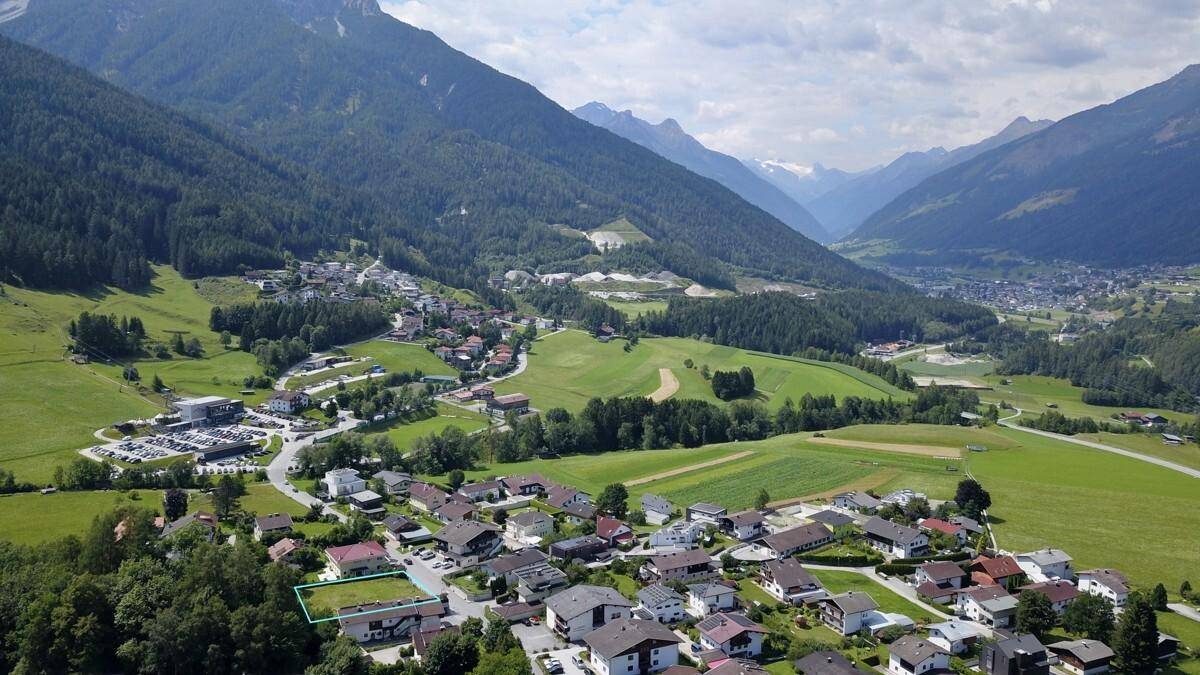 Panoramische Luftaufnahme eines Tals mit einem Dorf, umgeben von majestätischen Bergen und grünen Wäldern.